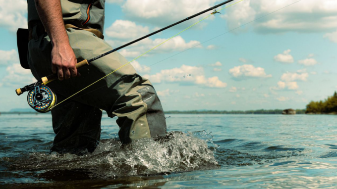 a man fishing in a stream wearing waders and holding a fishing rod